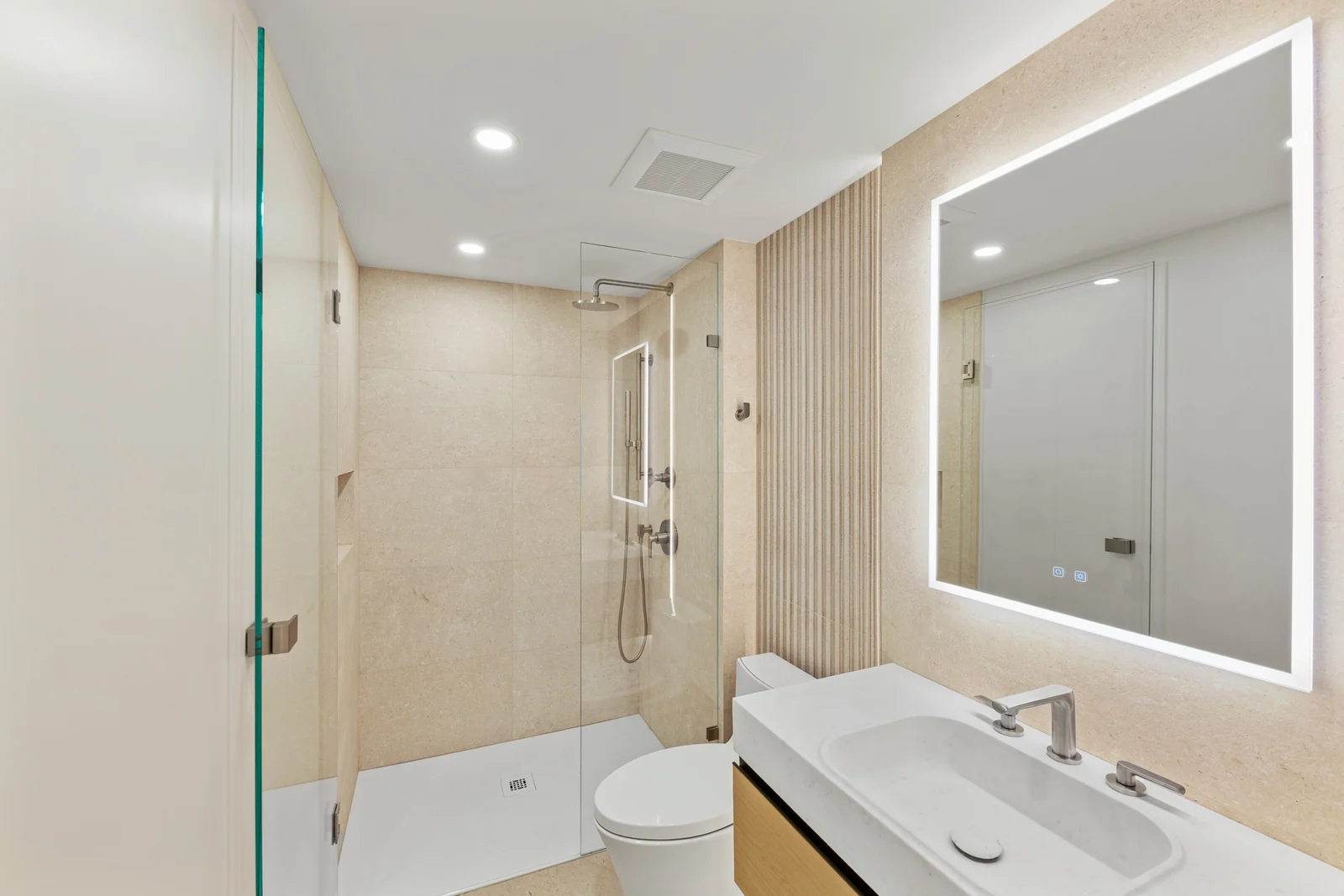 Finished modern bathroom with a glass walk-in shower, fluted wood wall, and illuminated mirror
