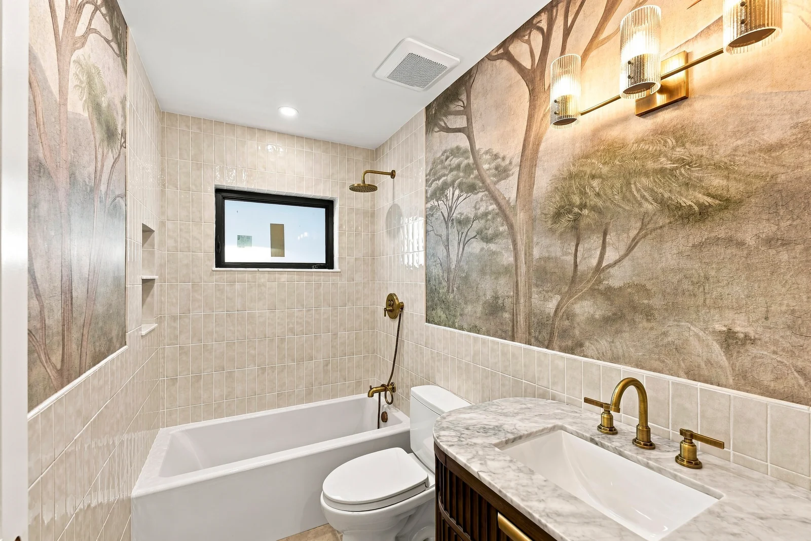 Finished bathroom with a botanical mural wall, white tub, marble vanity, and brass fixtures